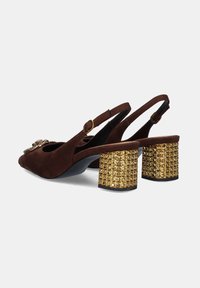 Zapatos slingback de ante marrón con un tacón de bloque adornado con clavos dorados y una embellecimiento decorativo en la parte delantera. Incluye una correa en el tobillo con hebilla.