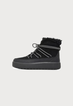 Botte d’hiver noire avec une semelle épaisse, des lacets noirs et blancs enroulés autour de la cheville, et une doublure en fourrure douce en haut.