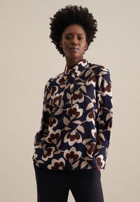 Blusa navy con motivo floreale in bianco, marrone e beige. Presenta un colletto, chiusura con bottoni e maniche lunghe. Tessuto dalla texture liscia.
