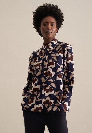 Blusa navy con motivo floreale in bianco, marrone e beige. Presenta un colletto, chiusura con bottoni e maniche lunghe. Tessuto dalla texture liscia.