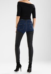 Jeans de cintura alta con un trasero de mezclilla y un frontal de piel sintética negra, que presentan un diseño elegante y dos bolsillos traseros. Tacones negros completan el conjunto.