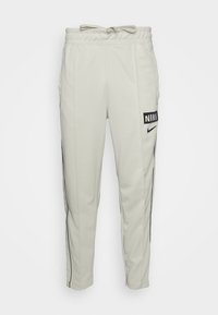 Ljusgrå Nike-byxor i mjukisstil med elastisk midja, dragsko, sidostripedetaljer och en framtr ädande svart Nike-logotyp på vänster lår.