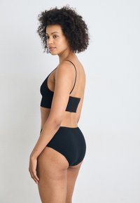 Zwarte bralette en hooggepaste onderbroek van zacht materiaal. Heeft dunne bandjes en een naadloos ontwerp voor comfort. Zijaanzicht weergegeven.