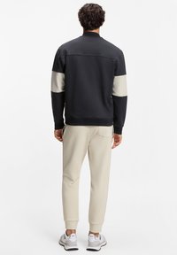 Schwarz- und cremefarbenes Sweatshirt mit hohem Kragen, glatter Textur und gerippten Bündchen, kombiniert mit hellbeigen Jogginghosen und grauen Turnschuhen.