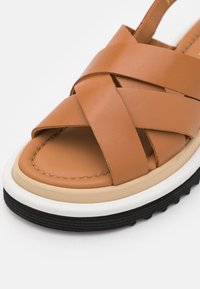 Sandale en cuir camel avec des brides croisées, une semelle intérieure rembourrée, une semelle intermédiaire beige et une semelle extérieure noire texturée.