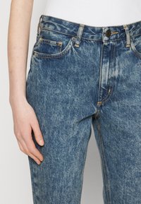 Světlemodré džíny z denimu s vybledlým efektem, rovného střihu, s pěti kapsami a žlutým prošitím na švech a kapsách.