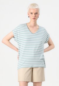 Lys blå og hvid stribet kortærmet V-hals top med en afslappet pasform og blød tekstur, parret med beige shorts.