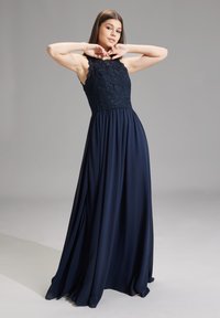 Marineblaue Abendkleid mit Spitze und ärmellosem Design. Fließender Rock aus leichtem Stoff, mit gerafftem Bund und subtilem Drapieren.