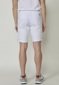 Shorts en coton blanc avec un ourlet retroussé, poches arrière plates et une branding discrète. Associés à des baskets grises et bleues.