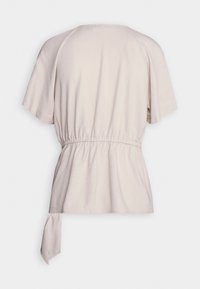 Blusa corta de manga corta en color beige claro con una cintura ceñida y un detalle de lazo en la parte posterior. Tejido suave con una textura lisa.