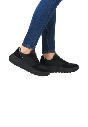 Baskets de sport noires avec une semelle en caoutchouc texturée, une tige en suède et en tissu, et un laçage à l'avant. Présente des accents brillants et un design imposant.