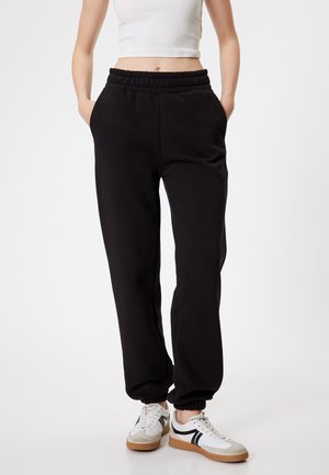 Zwarte trainingsbroek met een elastische tailleband, zijzakken, tapse boorden en zachte katoenmix stof, gecombineerd met witte sneakers.