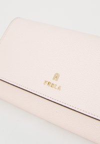 Lichtroze gestructureerde leren portemonnee met een gouden "Furla" logo, gedetailleerde stiknaden en een slank, rechthoekig ontwerp.