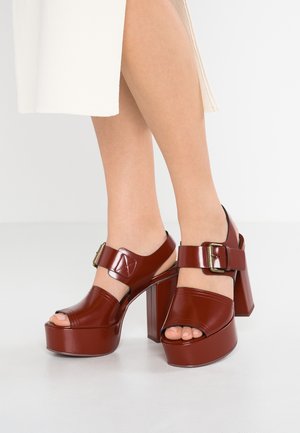 Rode platformhakken van lakleer met enkelbandje en gesp. Beschikken over een afgeronde open neus en een grote blokhak. Glad, glanzend oppervlak.