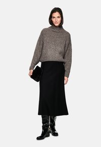 Pull en maille marron à col haut, jupe midi noire et bottes noires en cuir laqué jusqu'au genou. Une pochette en fourrure noire complète l'ensemble.