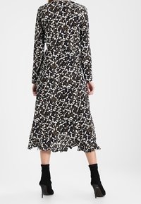 Långärmad klänning med svart bas och vitt blommönster, cinchad midja och volangkant. Bärs med ankelboots.