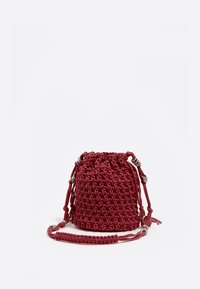 Bolso bandolera tejido en rojo con cierre de cordón, que presenta correas trenzadas y acentos metálicos. Forma redondeada, superficie texturizada.
