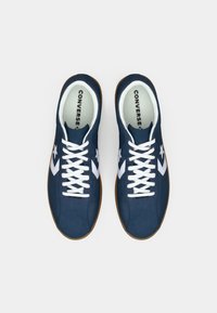Zapatillas de deporte de color azul marino, hechas de ante, con detalles y cordones en blanco, suela de goma y logo en la plantilla. Diseño atlético clásico.