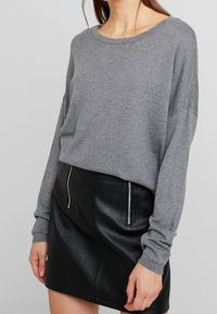 Harmaa neulepaita pyöreällä pääntiellä ja pitkillä hihoilla, yhdistettynä mustaan tekonahkaiseen mini-hameeseen, jossa on sivuvetoketju.