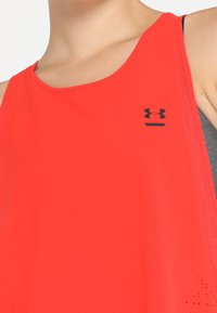 Red sleeveless athletic tank top made of smooth fabric, featuring a black Under Armour logo and small perforations near the hem.