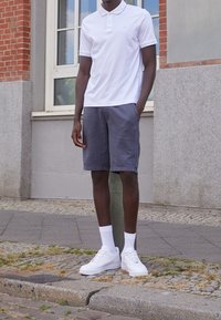 Vit pikétröja, grå shorts med sidofickor och vita sneakers med texturerade sulor. Shortsen har broderad logotypdetalj.