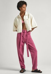 Krémová košile s krátkým rukávem a texturou, růžový crop top, volné růžové kalhoty s opaskem a černé pantofle.
