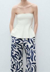 Halenka bez ramínek krémové barvy s peplum lemem v kombinaci s kalhotami širokého střihu s námořnickým abstraktním vzorem na krémovém pozadí.