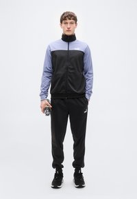 Μαύρη και λεβαντίν φόρμα αθλητικής χρήσης με ζακέτα με φερμουάρ και παντελόνι με ελαστική μέση. Διαθέτει λεπτομέρειες με λογότυπο και απαλή υφή υφάσματος.