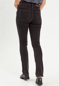 Jean en denim noir avec une coupe slim, comprenant deux poches arrière et des accents de couture. Le matériau a une texture lisse avec un minimum d'élasticité.
