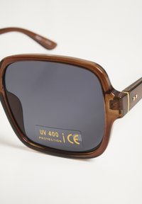 Rjave, velika kvadratna sončna očala s temnimi lečami, na katerih je prikazan napis o UV 400 zaščiti in certifikatu CE.