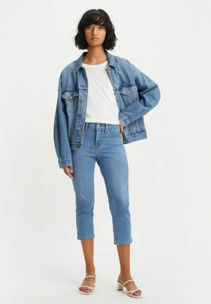 Jeansjacka och ljusblå jeans med avklippta ben. Outfiten inkluderar en vit t-shirt och beige klackar med remmar. Ljus tvättad denim genomgående.