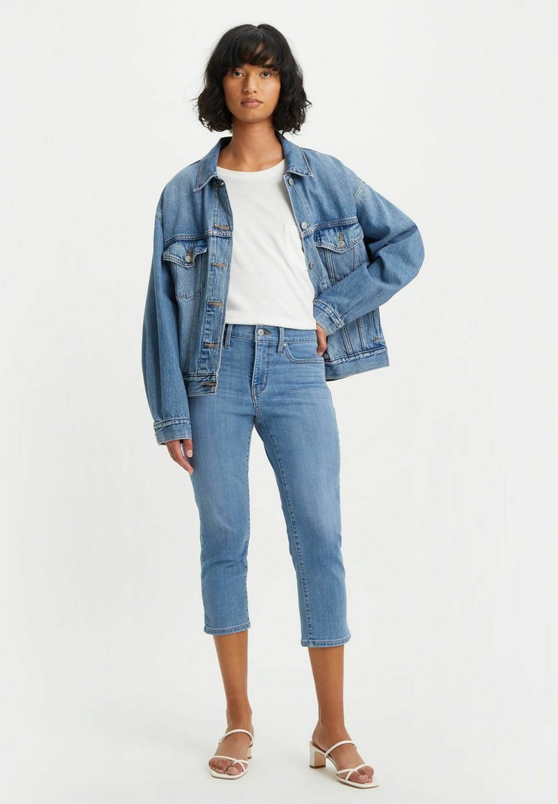 Denim jacket and light blue jeans with cropped legs. The outfit includes a white t-shirt and beige strappy heels. Light wash denim throughout.