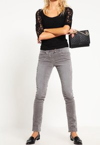 Svart spetsblus, grå kordruffstygbyxor och svarta loafers. Handväskan har en kviltad design och en kedja för axeln.