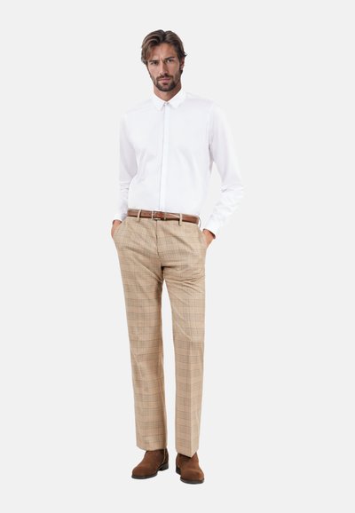 Chemise blanche à boutons, pantalon à carreaux beiges, ceinture en cuir marron et bottines en suède marron. Coupe standard avec manches longues et col.