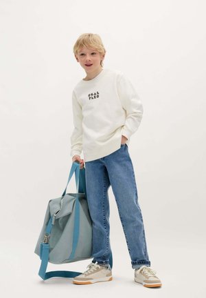 Lichtbeige sweatshirt met zwarte tekst, blauwe denim jeans en beige sneakers. Draagt een grijze stoffen rugzak met blauwe banden en een rits.