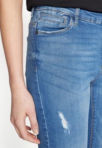 Svijetloplave traperice od denima, sa slim fit krojem, prednjim džepovima i ispucalom detaljem na butu.
