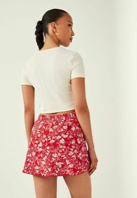 Hvid ribbet crop top parret med en rød nederdel med blomsterprint, der har en elastisk talje og en trompetformet silhuet.