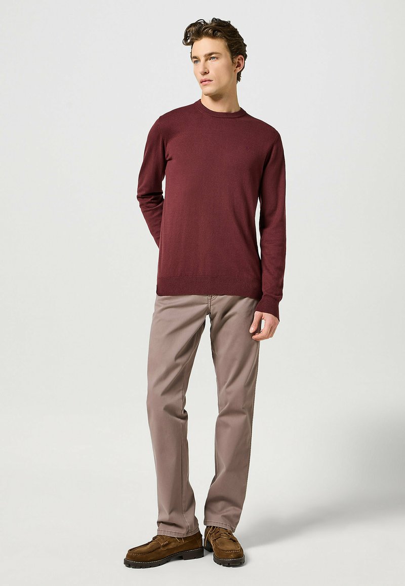 Maglione a maniche lunghe bordeaux, colletto tondo, abbinato a pantaloni chinos marrone chiaro e scarpe in suede marroni, con una texture minimale e un design aderente.