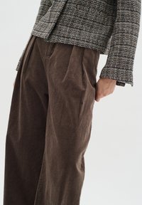 Pantaloni in corduroy marrone testurizzato abbinati a una giacca a motivo multicolore, caratterizzata da una silhouette aderente e maniche a campana.