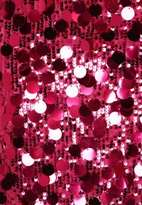 Tessuto rosa acceso con paillettes circolari in varie tonalità di rosa e rosso, che riflettendo la luce mostrano una texture lucida.