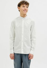 Camicia chiara a maniche lunghe con colletto alla coreana. Realizzata in tessuto testurizzato. Abbinata a pantaloni grigi.