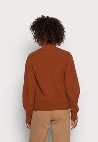 Hnědo-oranžový, pohodlný svetr s vysokým límcem a balónovými rukávy. Má žebrovaný lem a manžety, vyrobený z měkké, strukturované tkaniny.