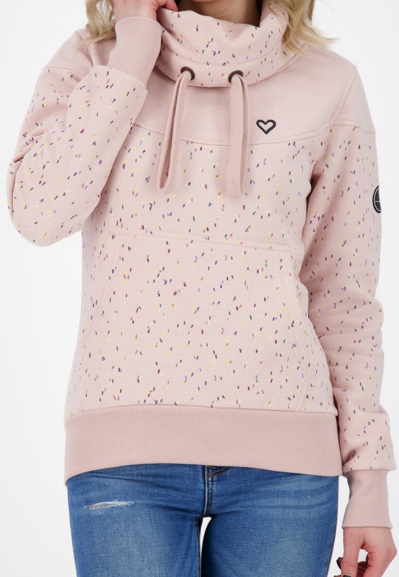 Světle růžová mikina s vysokým límcem, s tečkovaným vzorem v různých barvách, žebrovanými manžetami a přední kapsou. Detail černého srdíčka.loga.