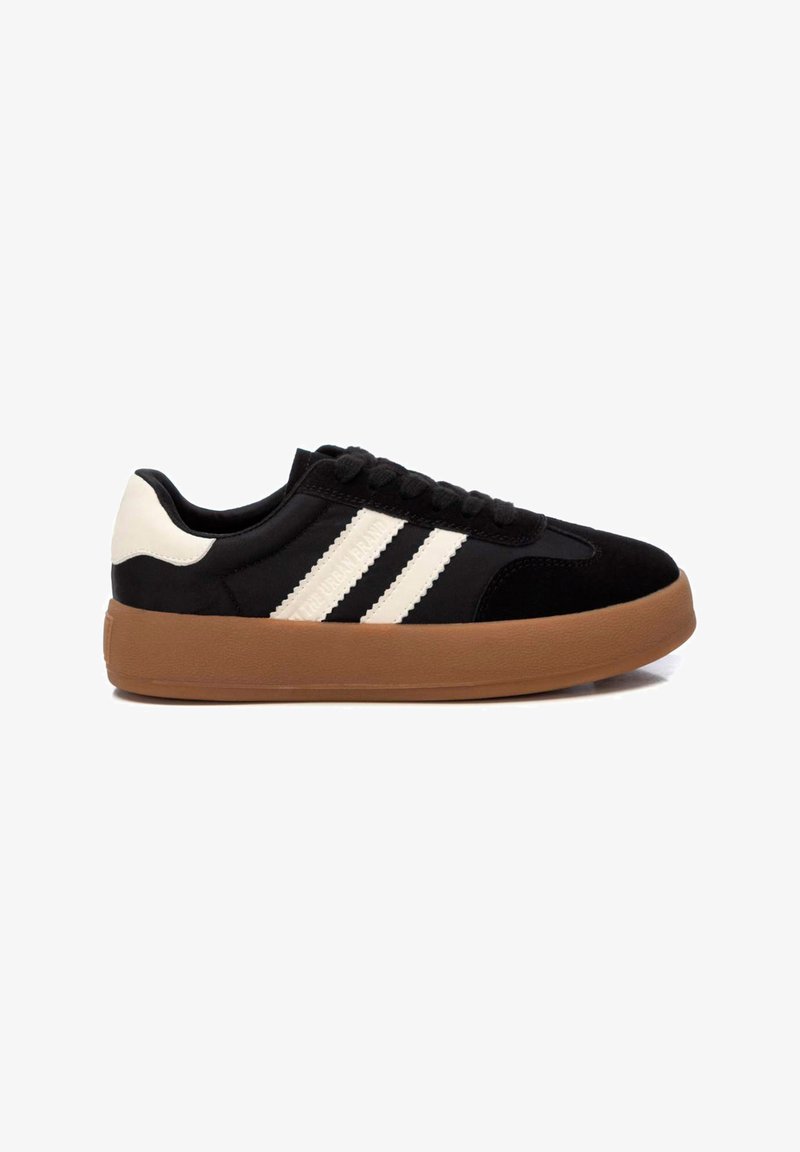 Zapatilla de ante negra con rayas blancas, punta redonda, suela plana de goma marrón y cordones negros. Textura suave con acentos en contraste.