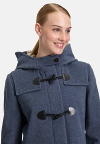 Tengerészkék gyapjú kabát kapucnival, kapcsolókkal, nagy elülső zsebekkel és strukturált felülettel. Egyszerű dizájn kontrasztos fekete részletekkel.