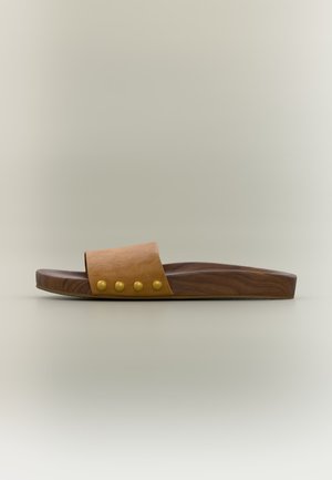 Jedna hnedá šľapka so širokým koženým remienkom a štyrmi okrúhlymi zlatými cvokmi, podrážka s drevenou textúrou, minimalistické pozadie.