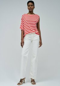 Blusa de rayas rojas y blancas, de corte holgado, combinada con pantalones rectos blancos y sandalias de tacón beige, sobre un fondo neutro.