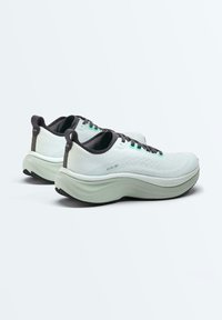 Paire de chaussures de sport blanches avec semelles épaisses rembourrées, doublure intérieure noire et lacets noirs sur un fond clair uni.