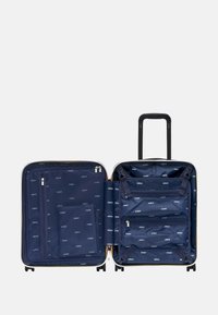 Valigia rigida con interno blu navy che presenta motivi con logo, più scomparti, tasche con zip e una maniglia retrattile nera.