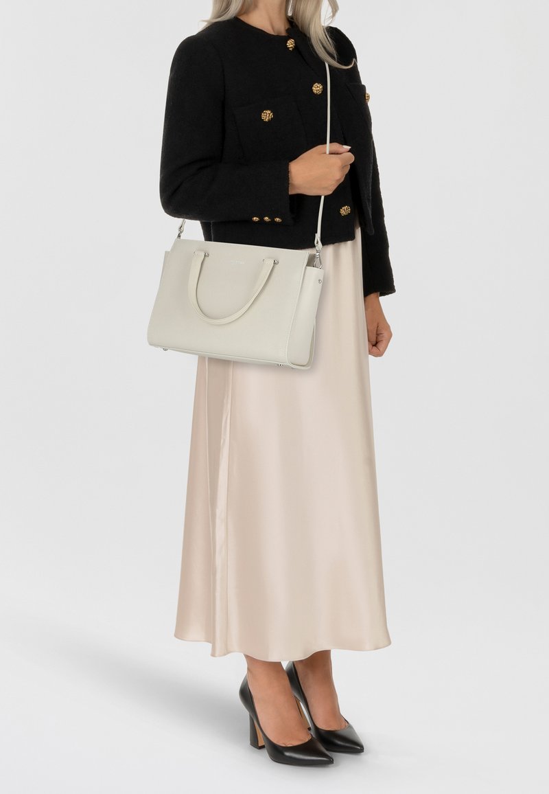 Bolso de mano de cuero blanco con asas dobles, forma estructurada y herrajes de plata. Combinado con una chaqueta corta negra y un vestido de satén beige.